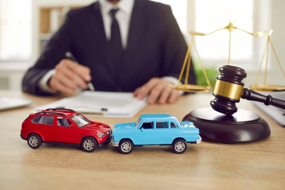 Car accident lawyer reviewing case documents with toy cars and a gavel on desk symbolizing legal help after a car crash.
