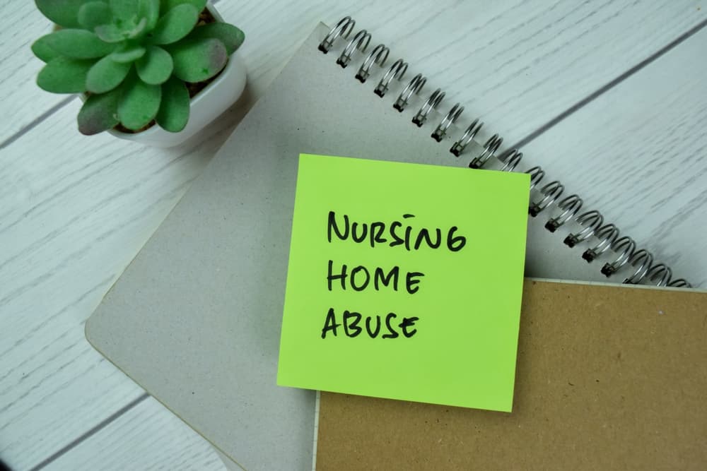 Concept of Nursing Home Abuse write on sticky notes isolated on Wooden Table.