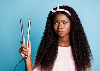 Black woman holding hair straightener skeptically