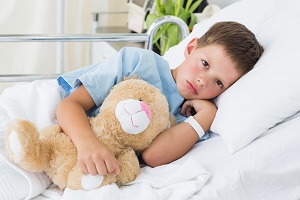 Little boy with teddy bear waits in hospital bed