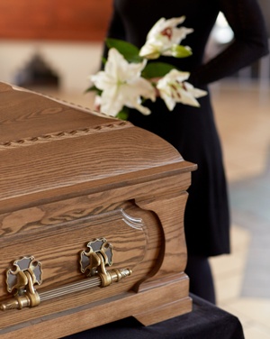 casket with woman holding lilies in the background