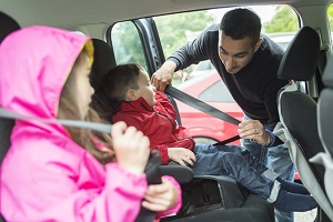 Dad buckles the kids into their safety seats in the car