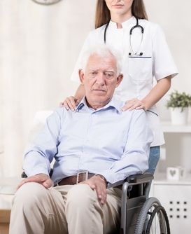 Elderly man in wheelchair being pushed by a female healthcare worker