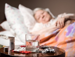elderly woman in bed looking at table of medication