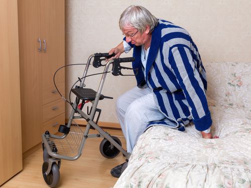 Elderly man leaning on rolling walker to get out of bed