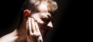 man-holding-ear-in-pain-black-background